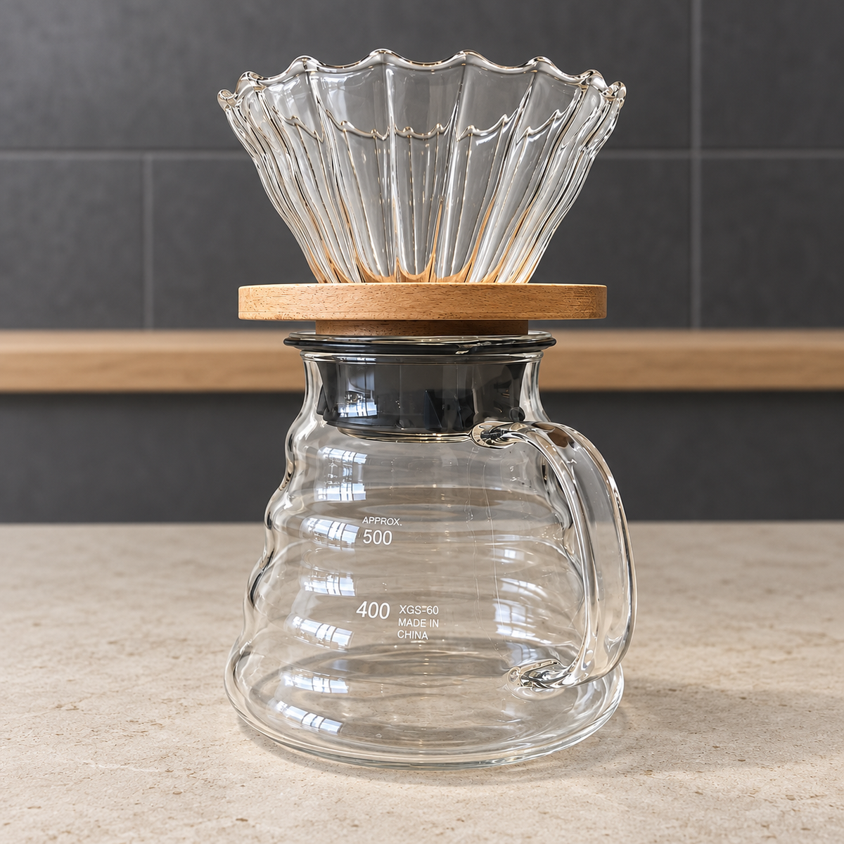 Kit V60 de vidrio con base de madera y server sobre una mesa de preparación con luz suave.